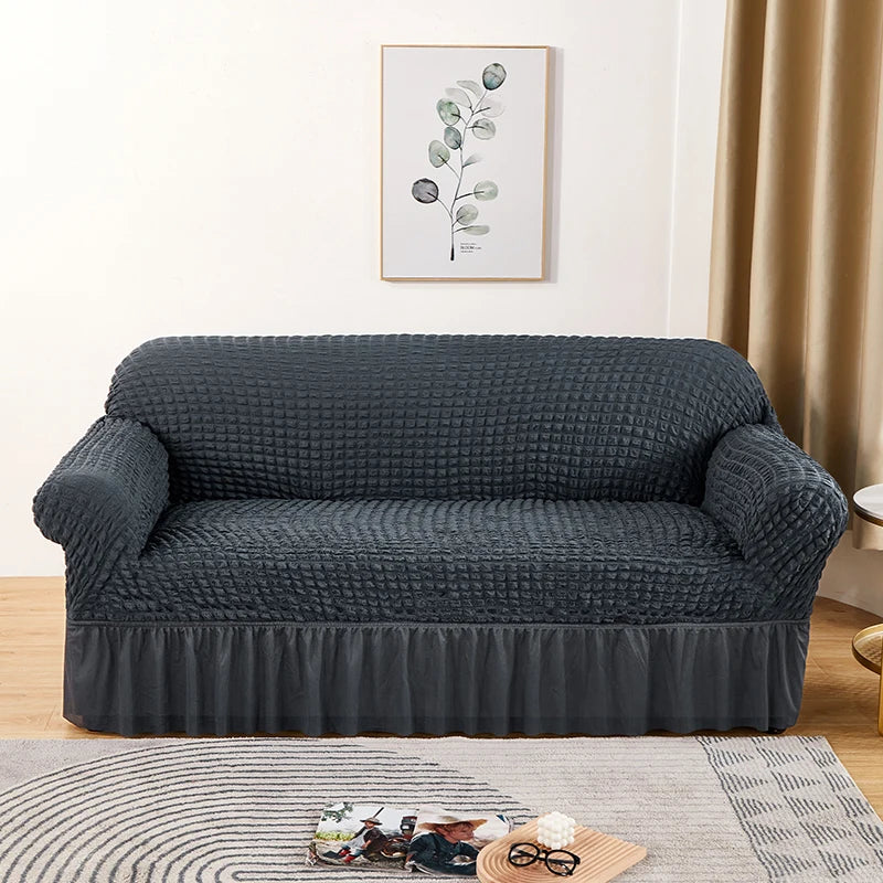 Stretchable sofa cover in a neutral tone, fitting snugly over a three-seater couch, providing protection and a refreshed look to the living room furniture