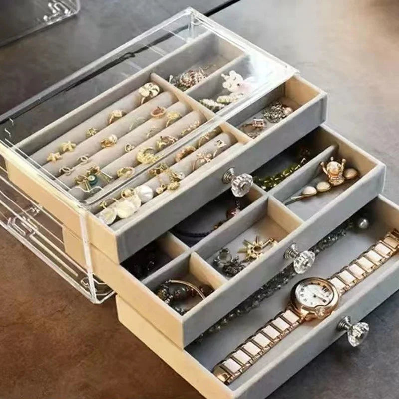 A clear acrylic jewelry organizer featuring multiple compartments and drawers, designed to neatly store and display rings, necklaces, bracelets, and earrings. Its transparent design allows for easy visibility of contents, while the compact structure fits seamlessly on a vanity or dresser, keeping accessories organized and easily accessible.