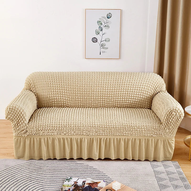 Stretchable sofa cover in a neutral tone, fitting snugly over a three-seater couch, providing protection and a refreshed look to the living room furniture