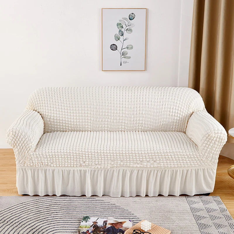 Stretchable sofa cover in a neutral tone, fitting snugly over a three-seater couch, providing protection and a refreshed look to the living room furniture