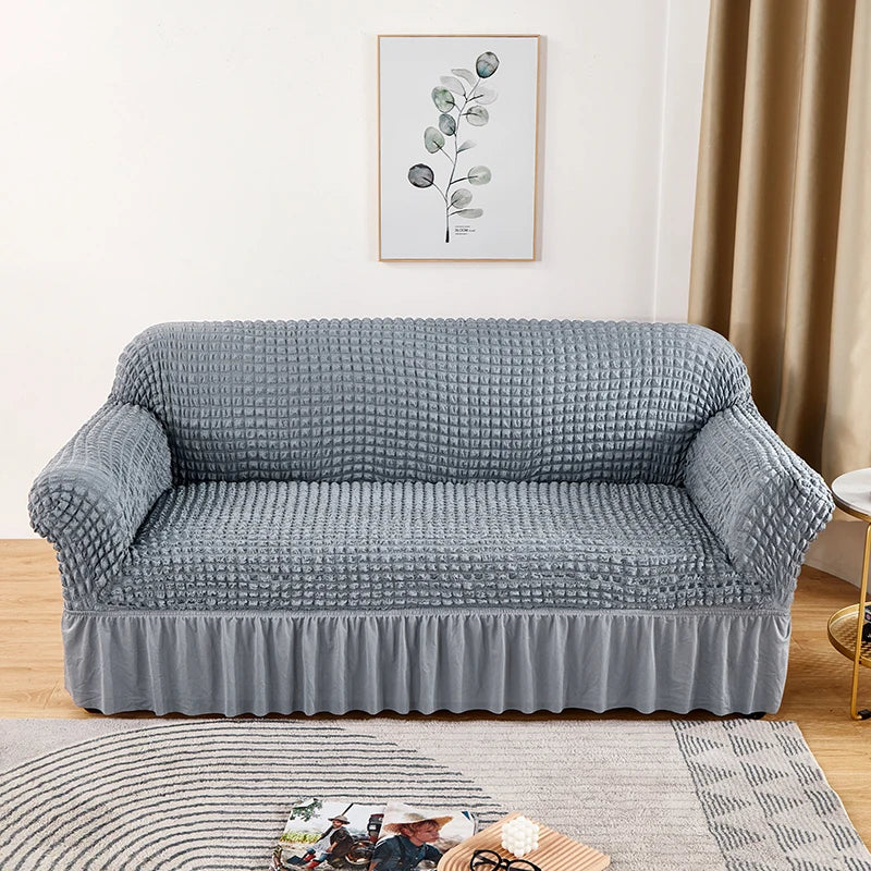 Stretchable sofa cover in a neutral tone, fitting snugly over a three-seater couch, providing protection and a refreshed look to the living room furniture