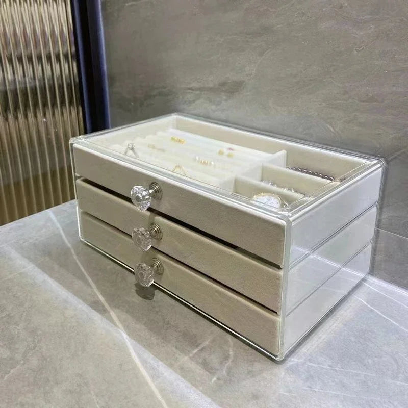 A clear acrylic jewelry organizer featuring multiple compartments and drawers, designed to neatly store and display rings, necklaces, bracelets, and earrings. Its transparent design allows for easy visibility of contents, while the compact structure fits seamlessly on a vanity or dresser, keeping accessories organized and easily accessible