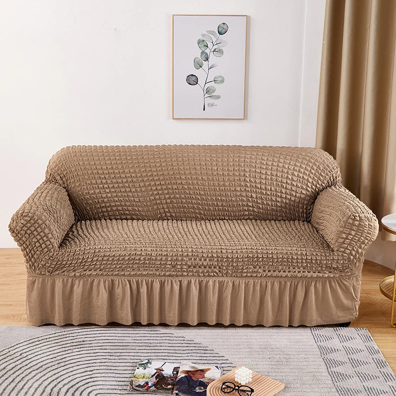 Stretchable sofa cover in a neutral tone, fitting snugly over a three-seater couch, providing protection and a refreshed look to the living room furniture