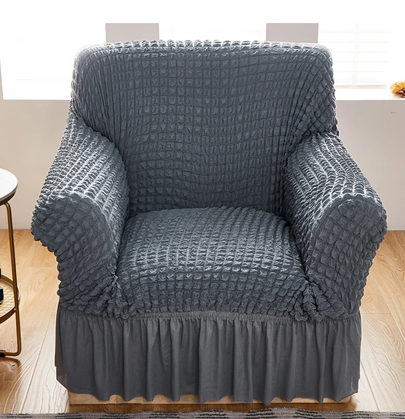 Stretchable sofa cover in a neutral tone, fitting snugly over a three-seater couch, providing protection and a refreshed look to the living room furniture