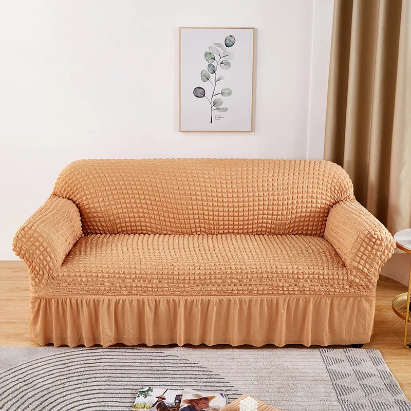 Stretchable sofa cover in a neutral tone, fitting snugly over a three-seater couch, providing protection and a refreshed look to the living room furniture