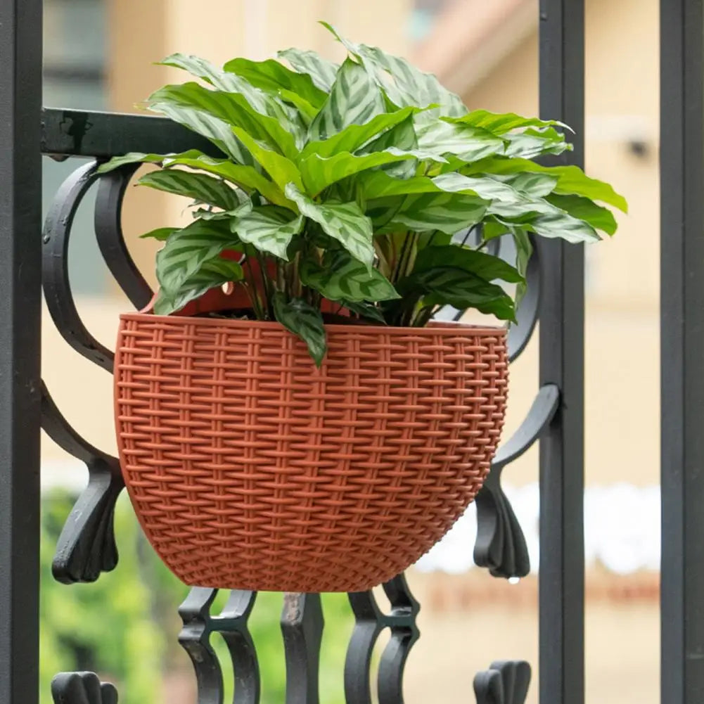 A durable plastic wall-mounted hanging planter in a half-round design, securely attached to a balcony railing. It is filled with vibrant blooming flowers, adding a touch of nature and color to the outdoor space.