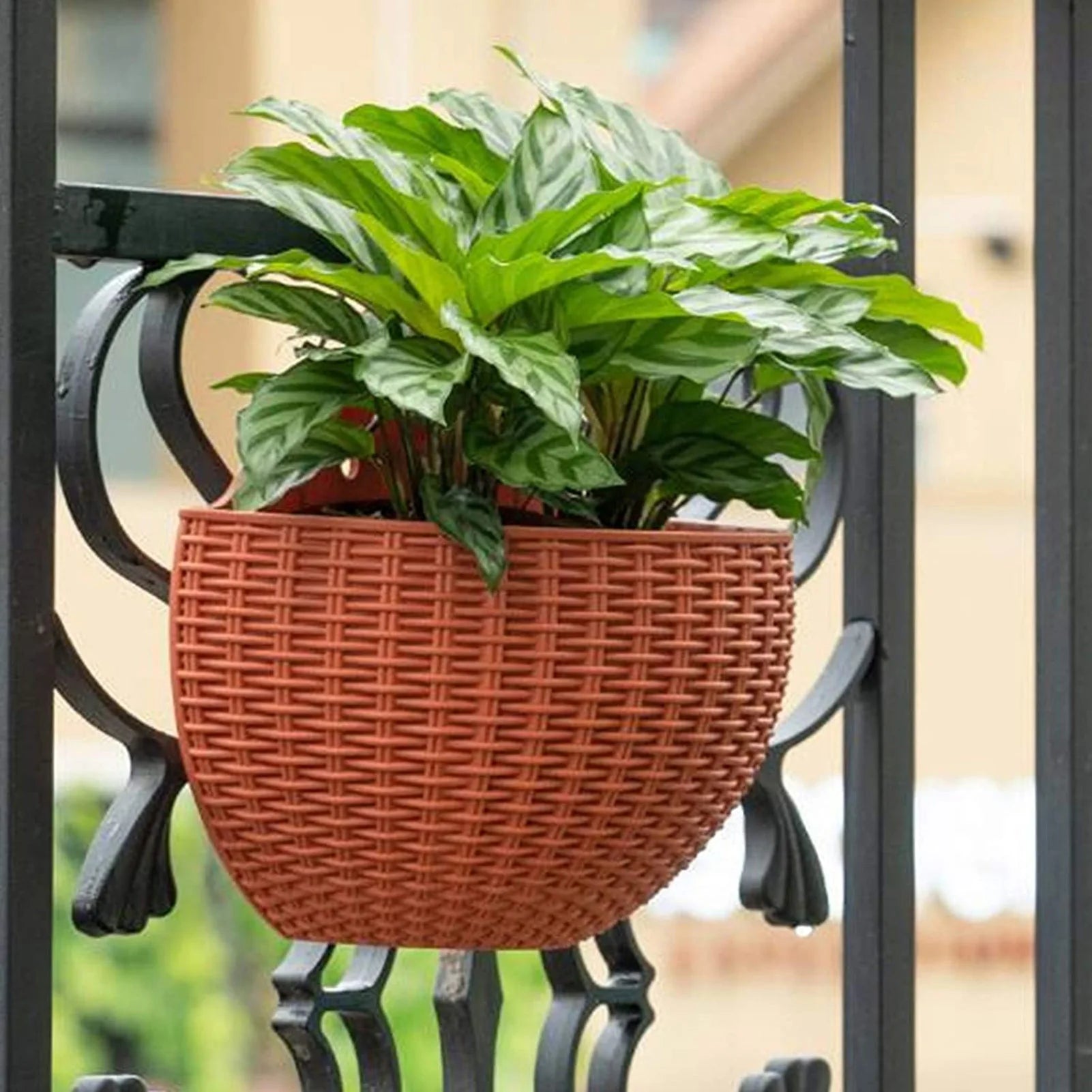 A durable plastic wall-mounted hanging planter in a half-round design, securely attached to a balcony railing. It is filled with vibrant blooming flowers, adding a touch of nature and color to the outdoor space.