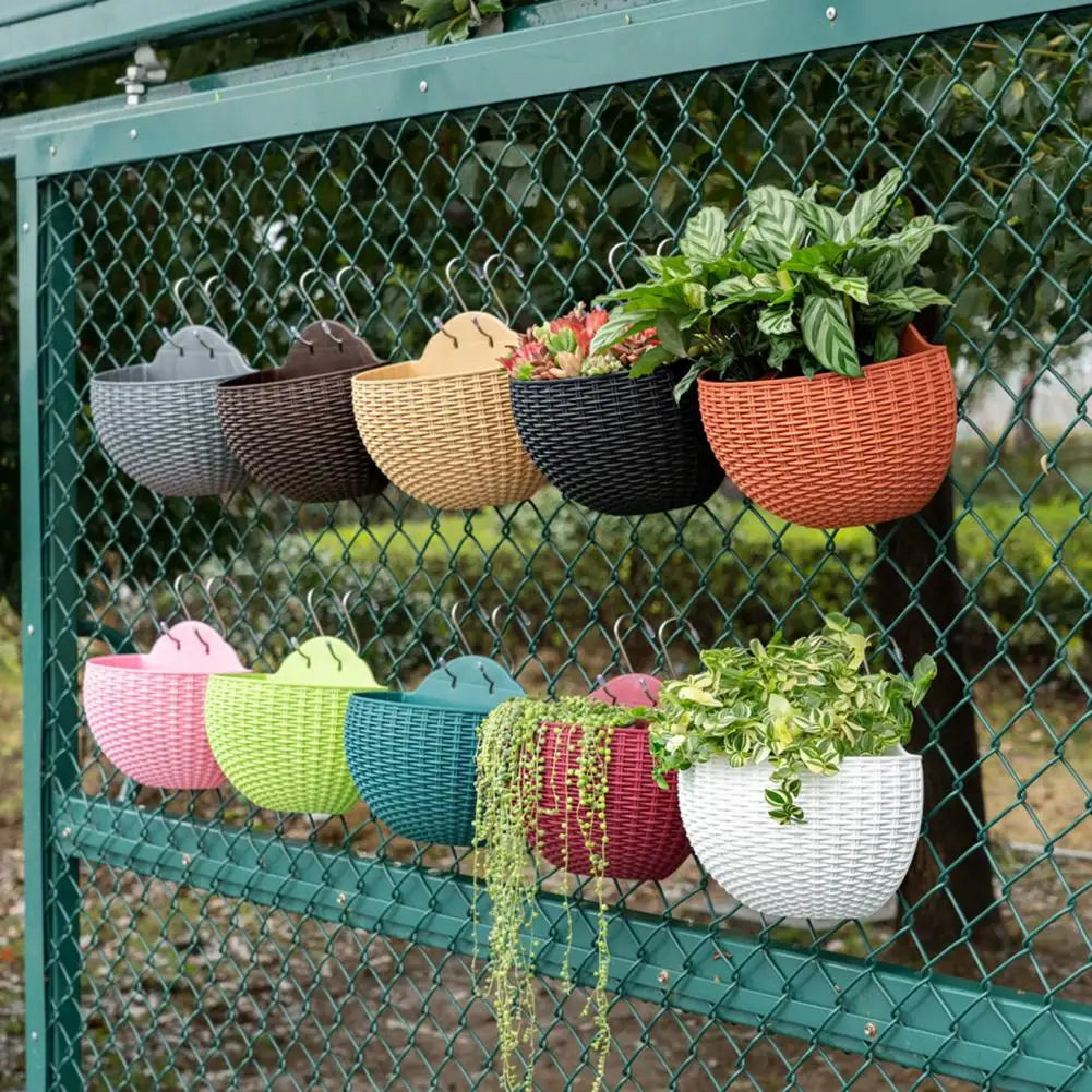 A durable plastic wall-mounted hanging planter in a half-round design, securely attached to a balcony railing. It is filled with vibrant blooming flowers, adding a touch of nature and color to the outdoor space.